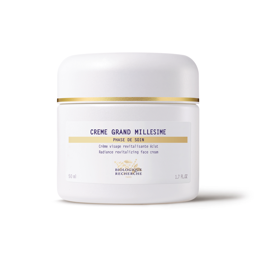 White jar of crème grand millesime with gold accents on a white background